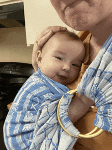 a woman is holding a baby in a sling and the baby is smiling