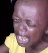 a close up of a baby 's face with a yellow shirt on crying .