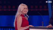 a woman in a red shirt is standing next to a man in a suit on a stage with a cbc logo in the background