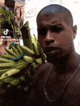 a shirtless man with a chain around his neck stands in front of a bunch of bananas and a plant