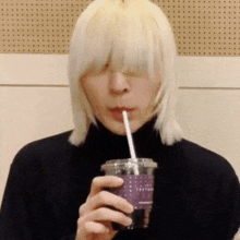 a man with blonde hair is drinking through a straw from a cup .