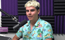 a man in a hawaiian shirt stands in front of a microphone in front of a sign that says offer for businesses