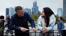 a man and a woman are standing next to each other on a fence with nbc written on the bottom