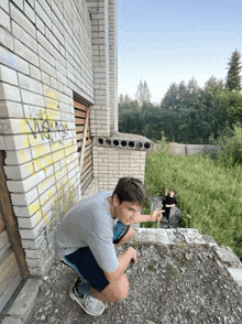 a boy squatting in front of a brick wall with graffiti on it that says ' nsm '