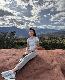 a woman sits on top of a rocky hill with mountains in the background