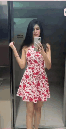 a woman in a red and white floral dress is taking a picture of herself in an elevator