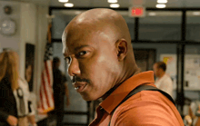 a man in an orange shirt stands in front of an exit sign