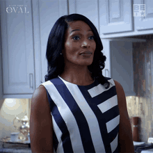 a woman in a blue and white striped dress is standing in a kitchen with oval written on the cabinets behind her