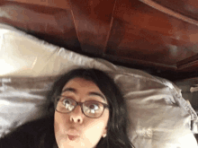 a woman wearing glasses is laying on a bed and making a funny face