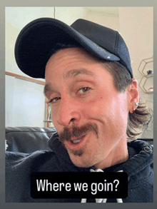 a man with a mustache is wearing a black hat and a black hoodie with the words " where we goin " on it