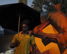 a man in a yellow polo shirt holding an umbrella stands in front of a painting