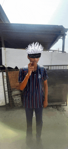 a boy wearing a striped shirt and sunglasses stands in front of a fence with a bag that says gk