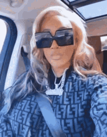 a woman is taking a selfie in a car wearing sunglasses and a necklace .