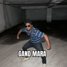 a man wearing sunglasses and a blue shirt is standing in a dark room with the words gand mara on the ground