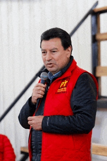 a man wearing a red vest that says pt on it holds a microphone