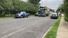 a garbage truck is driving down a street with a blue truck parked on the side of the road