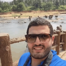 a man wearing sunglasses and a blue shirt is standing in front of a river