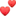 two red hearts are floating in the air on a white surface .