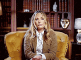 a woman is sitting in a chair in front of a bookshelf and a lamp .