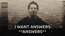 a man is standing in front of a brick wall with the words `` i want answers '' written on it .