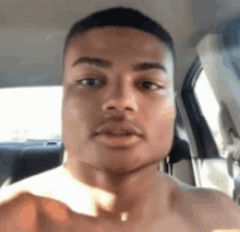 a shirtless man is sitting in the back seat of a car and making a funny face .