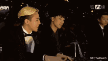 a man in a tuxedo is playing a piano in front of a screen that says mnet music video one