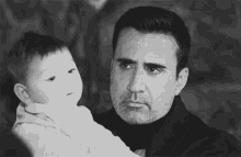 a man is holding a baby in his arms and looking at the camera .