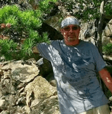 a man wearing sunglasses and a bandana is standing in front of a rocky cliff .