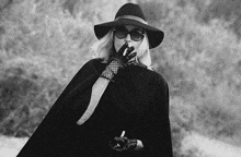 a woman in a hat and cape is smoking a cigarette and holding a knife in her hand .