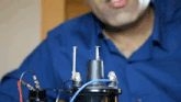 a man in a blue shirt is working on a device with wires and screws attached to it
