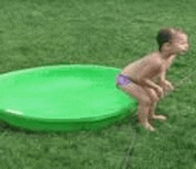 a little boy is squatting on top of a green swimming pool .