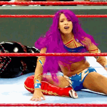 a female wrestler with purple hair is laying on the floor in a wrestling ring .