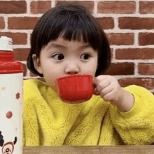 a little girl is drinking from a red cup while wearing a yellow sweater .