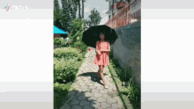 a woman in a pink dress is holding a black umbrella while walking down a path .