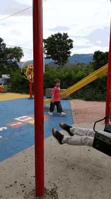 a little girl in a pink shirt stands next to a red pole with the letter d painted on it