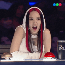 a woman with red and black hair is sitting at a table with a cup that says got on it