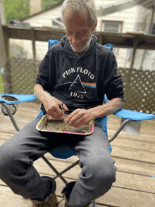 a man wearing a pink floyd 1973 shirt is rolling a joint