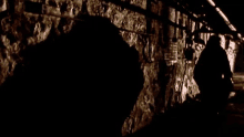 a shadow of a man is cast on a stone wall in a dark tunnel .