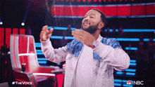 a man in a white and blue jacket is dancing on a stage with the nbc logo in the background