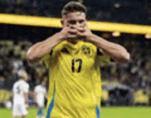 a soccer player wearing a yellow jersey with the number 17 on it is covering his face .