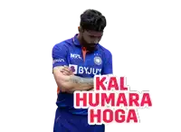 a man in a blue byju 's shirt stands with his arms crossed in front of a sign that says kal humara hoga