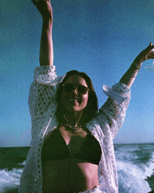 a woman in a bikini and sunglasses is holding a glass of wine in the air