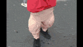 a person wearing a red shirt and a pair of black boots is walking down the street .