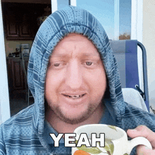 a man with a hood on his head is holding a coffee mug and saying yeah