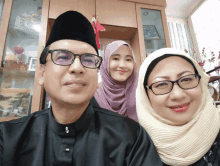 a man wearing glasses and a black hat poses for a photo with his wife and daughter