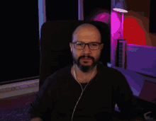 a bald man with glasses and a beard is wearing ear buds