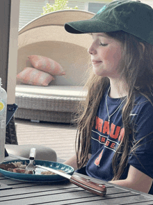 a girl wearing a blue shirt that says rau on it sits at a table with a plate of food