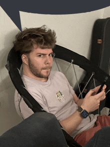 a man with a beard is sitting in a chair looking at his phone