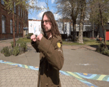 a man with long hair and glasses is standing in front of a building with a sign on it that says ' aa '