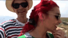 a man wearing a hat and sunglasses holds a woman with red hair